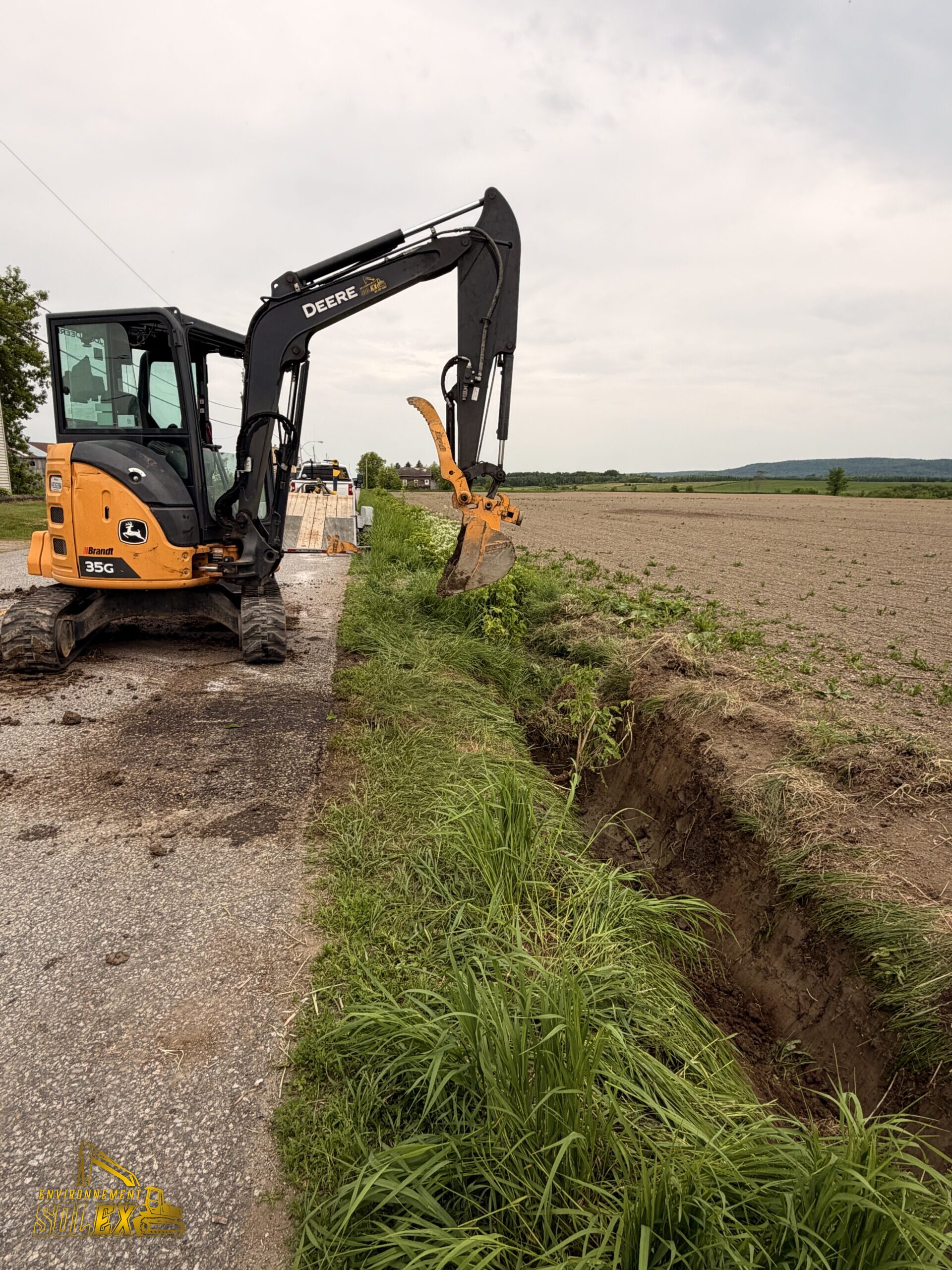 Mini-excavatrice creusant un fossé en bordure d'un champ