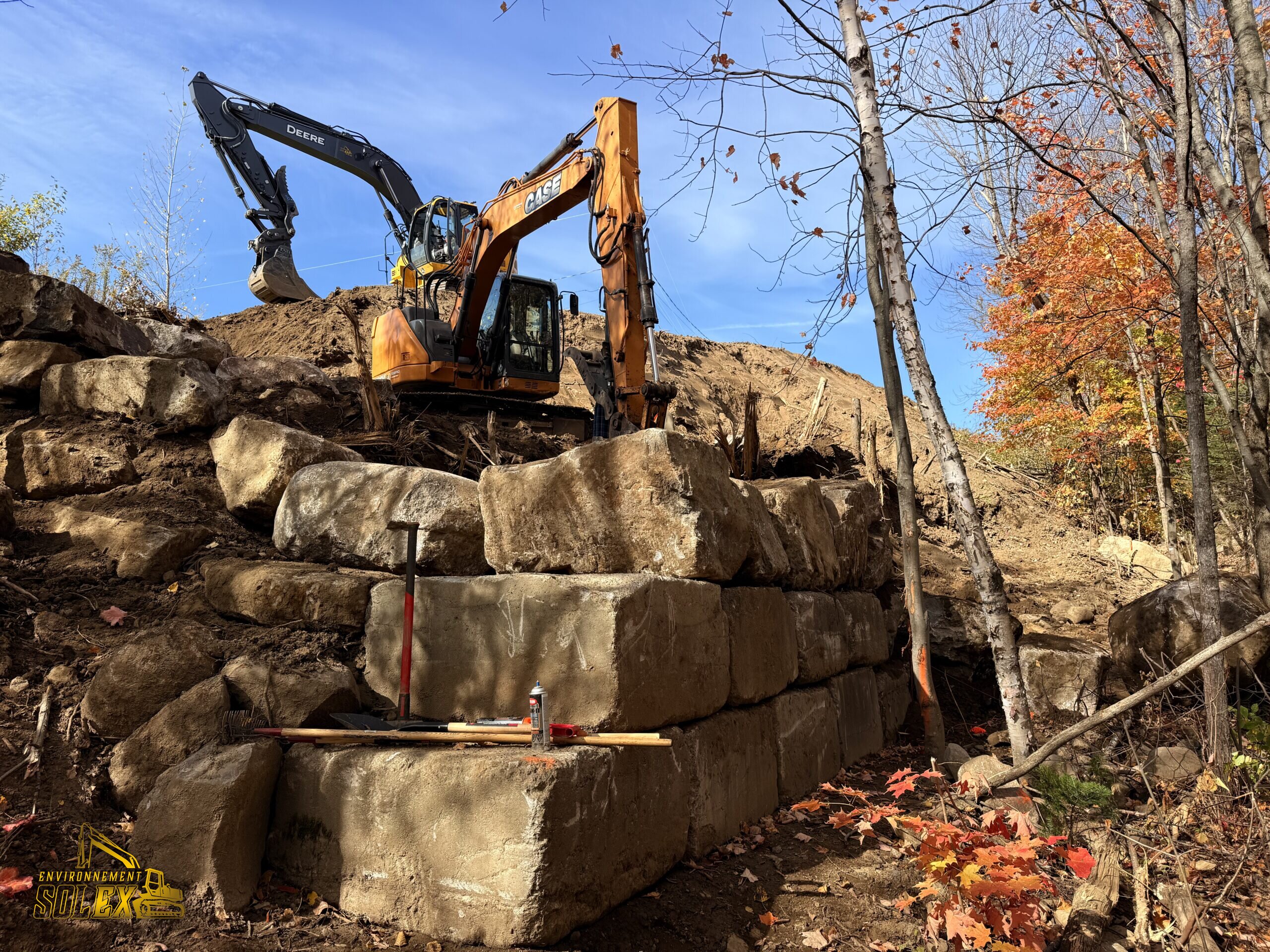 Excavatrice installant un mur de soutènement en blocs de pierre